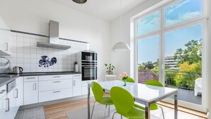 A modern kitchen with white cabinets, a black oven, and a large window with a view of greenery and buildings.