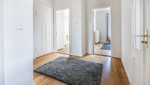 A hallway with white doors, a grey rug, and wooden flooring.