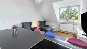 A modern loft bedroom with a sloped ceiling, a dining table, a small white side table, a floor lamp, and a window with a view of trees. - Apartment '4' with Wi-Fi (Heide)