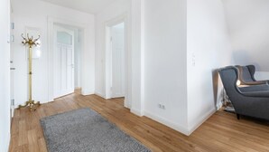 A spacious room with wooden flooring, a grey rug, a grey armchair, and a gold floor lamp. - Apartment '4' with Wi-Fi (Heide)
