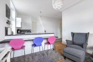 Een moderne keuken met een wit aanrecht, drie stoelen, een grijze fauteuil en een grijs vloerkleed.