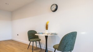 A dining area with a round table, two chairs, a vase with dried plants, and a wall clock. - Axis Apartment (Leeds)