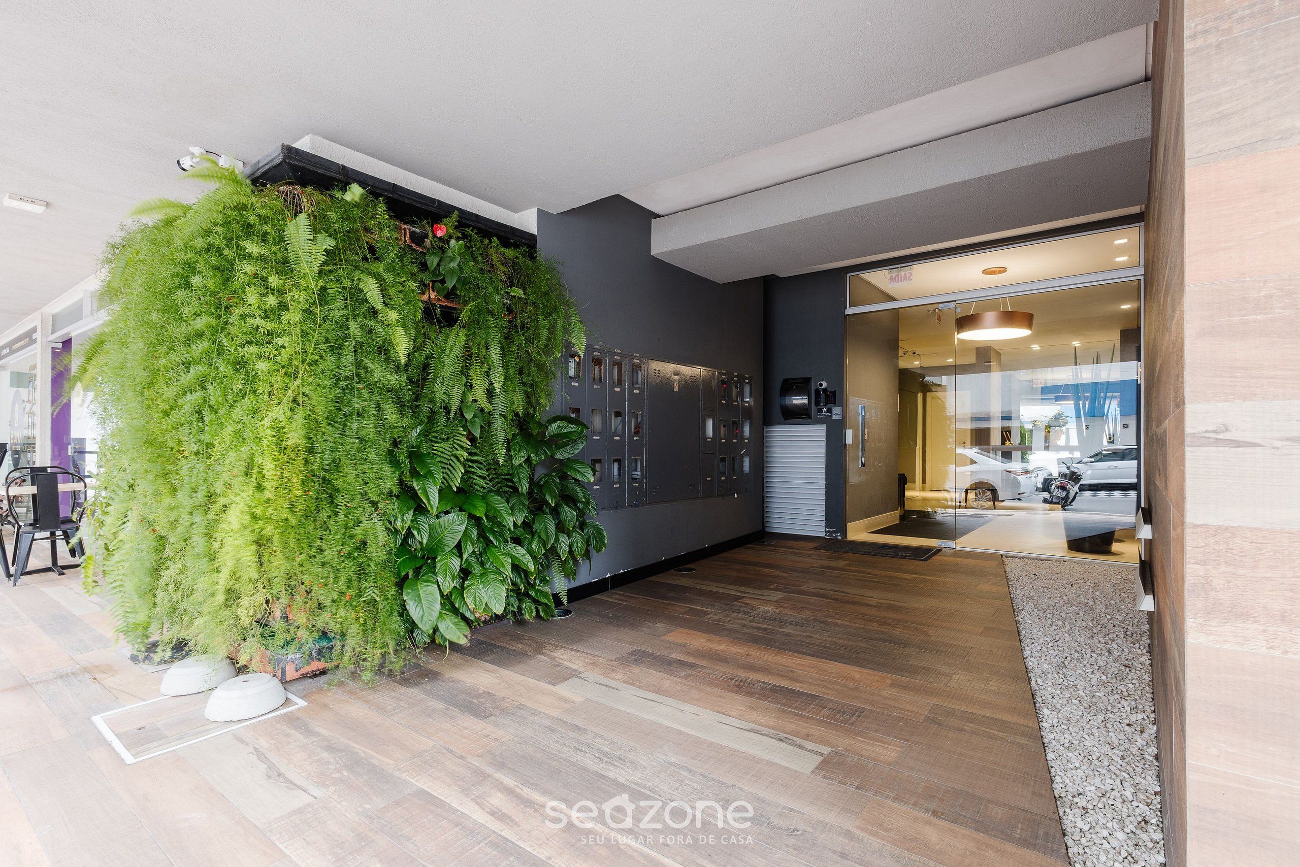 A modern interior with a large green wall, wooden flooring, and a reception area with a car visible outside.