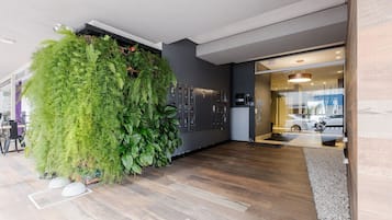A modern interior with a large green wall, wooden flooring, and a reception area with a car visible outside.