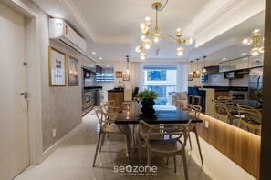 Une cuisine moderne avec un coin repas, comprenant un îlot central, des luminaires suspendus et une vue sur l’extérieur.