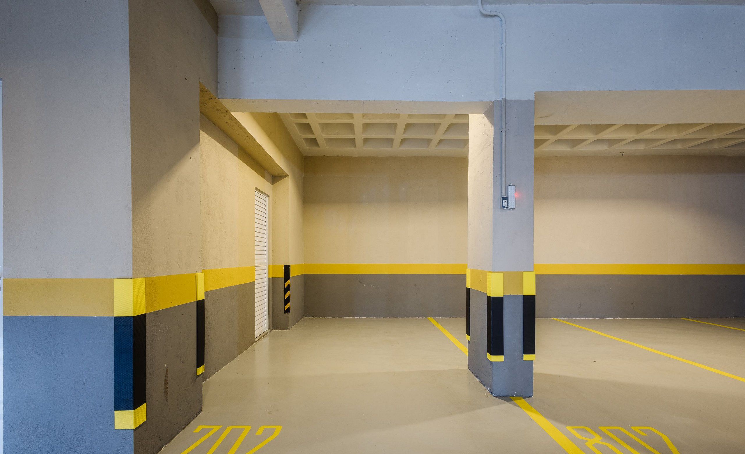 An empty parking garage with yellow and grey walls, concrete pillars, and floor markings.
