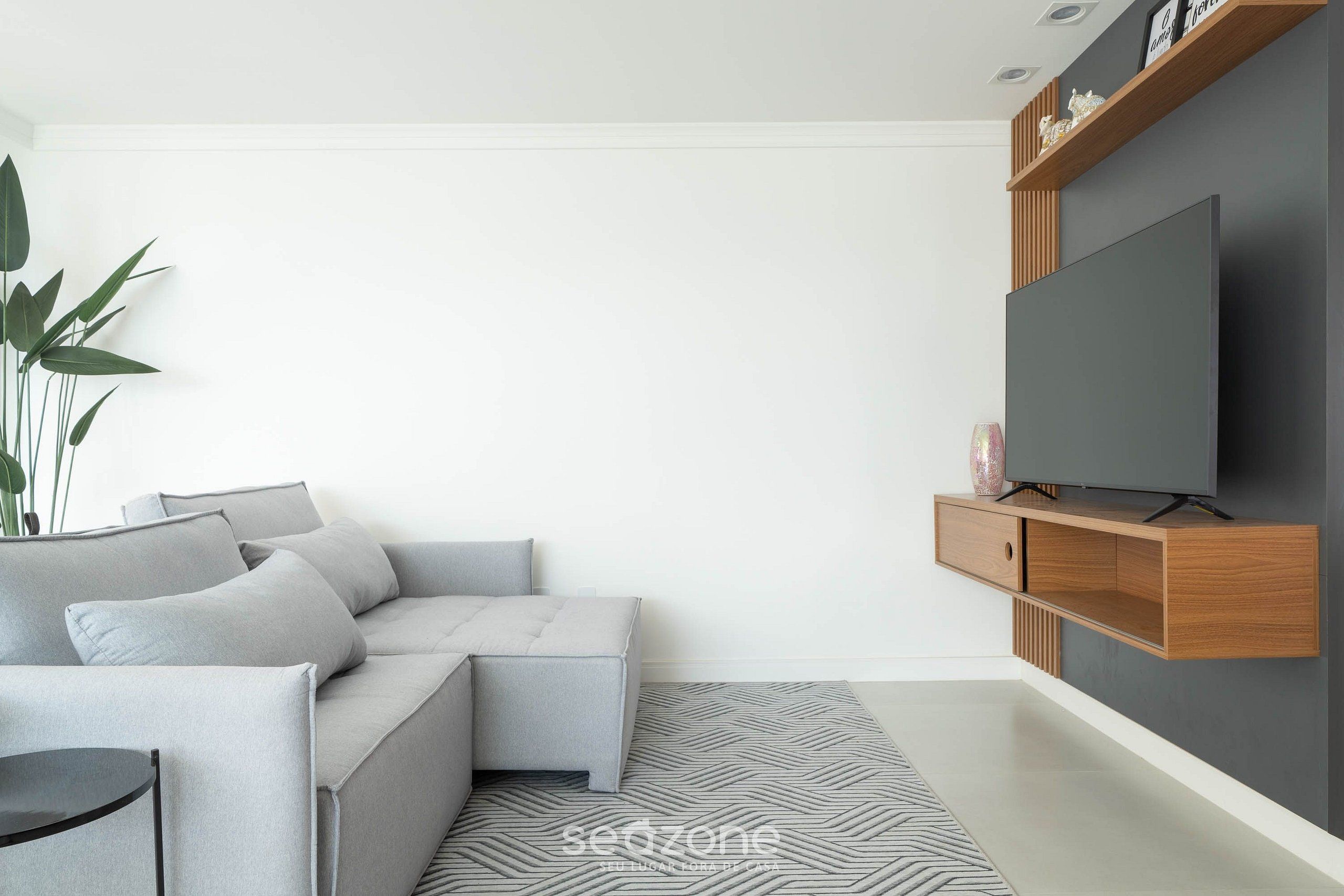 A modern living room with a grey sofa, a flat-screen TV mounted on a wooden console, and a patterned rug.