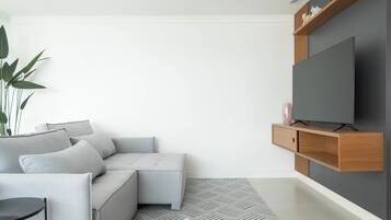 A modern living room with a grey sofa, a flat-screen TV mounted on a wooden console, and a patterned rug.