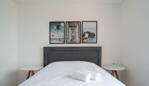 Una habitación de hotel con una cama, dos mesitas de noche y tres cuadros en la pared.