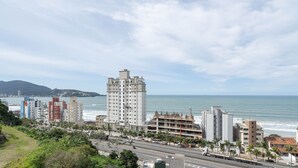 A coastal cityscape with a prominent white high-rise hotel, a busy street with vehicles, and a clear view of the ocean. - 2BR Seaview apt Near Itapema Beach Sem501 (Itapema)