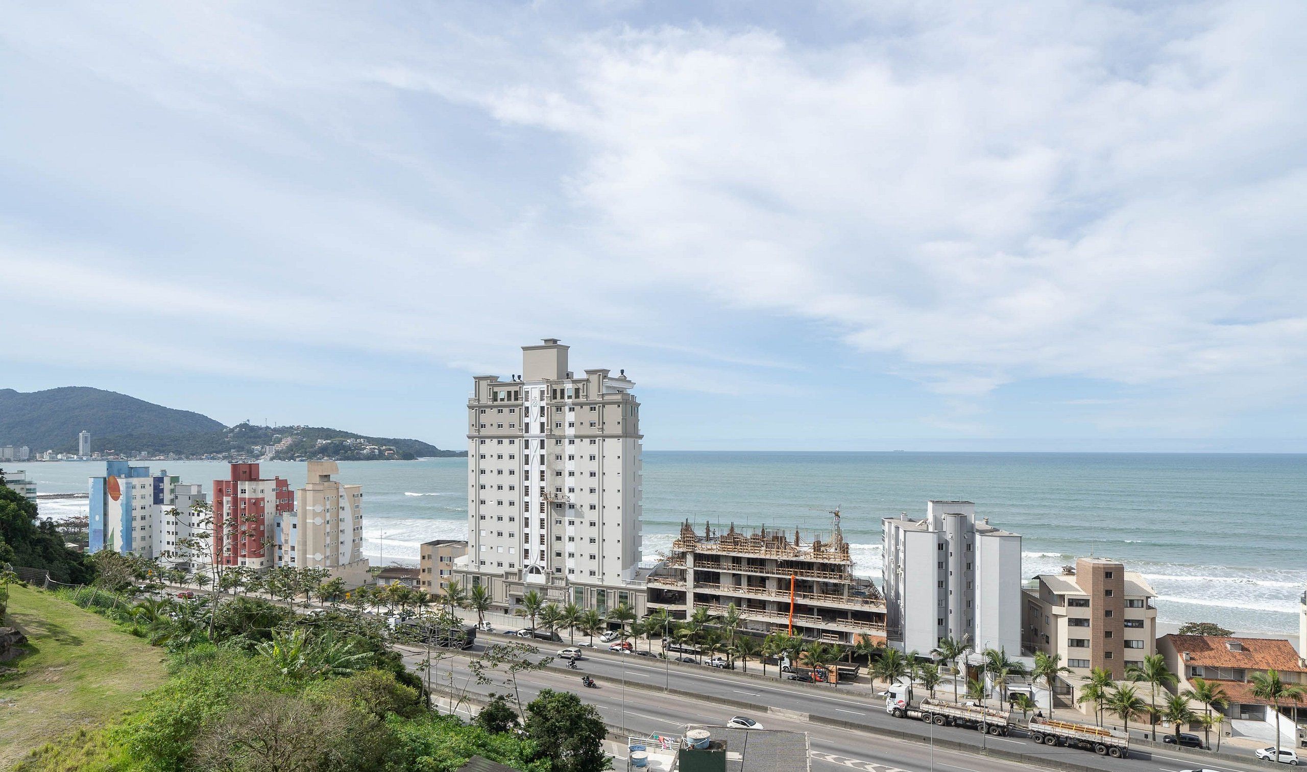 Un paisaje urbano costero con un hotel moderno blanco y visible, una calle concurrida con vehículos y una vista despejada del océano.