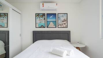 A hotel room with a bed, a bedside table with a phone, and wall art depicting a beach scene.