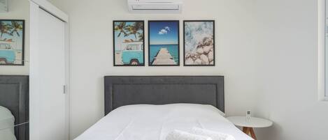 A hotel room with a bed, a bedside table with a phone, and wall art depicting a beach scene.