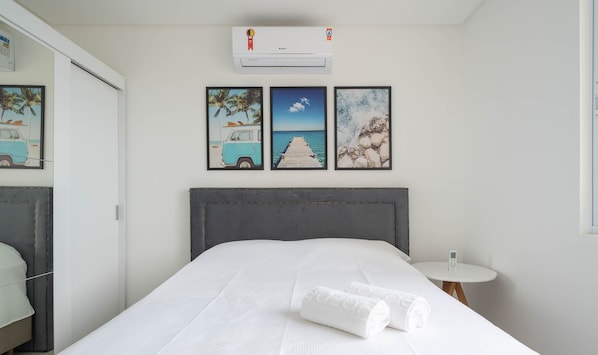 Una habitación de hotel con cama, mesita de noche con teléfono y una obra de arte en la pared que representa una playa.