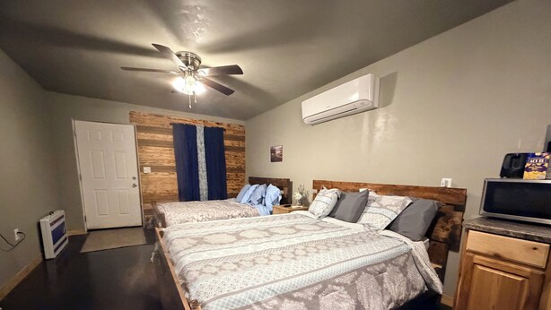 Un dormitorio con dos camas, ventilador de techo, aire acondicionado, cabecera de madera, televisor y un mueble pequeño.