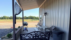Un patio cubierto con una parrilla, asientos al aire libre y un bote de basura.