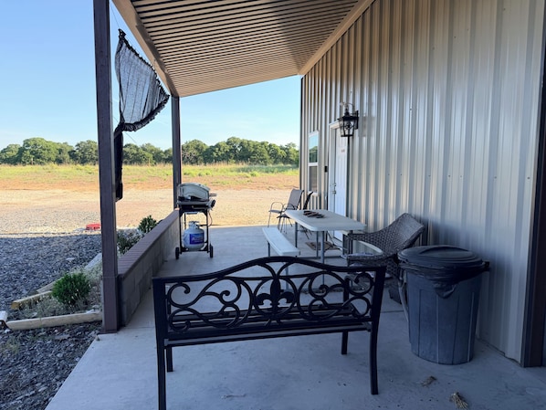 Un patio cubierto con una parrilla, asientos al aire libre y un bote de basura.