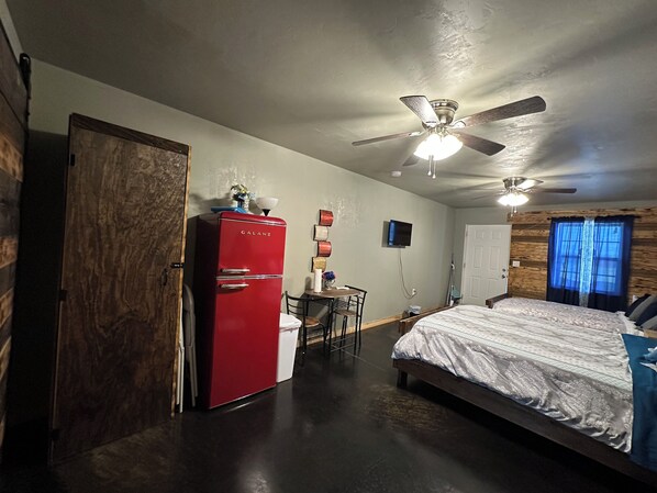 A bedroom with a bed, a red refrigerator, a ceiling fan, a wooden door, and a television on the wall. - Cozy Guest Room in awesome Kingston with AC close to lake Texoma Lots of parking (Kingston)