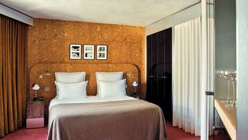 A hotel room with a bed, a nightstand, a mirror, a wall with photos, and a window with curtains.