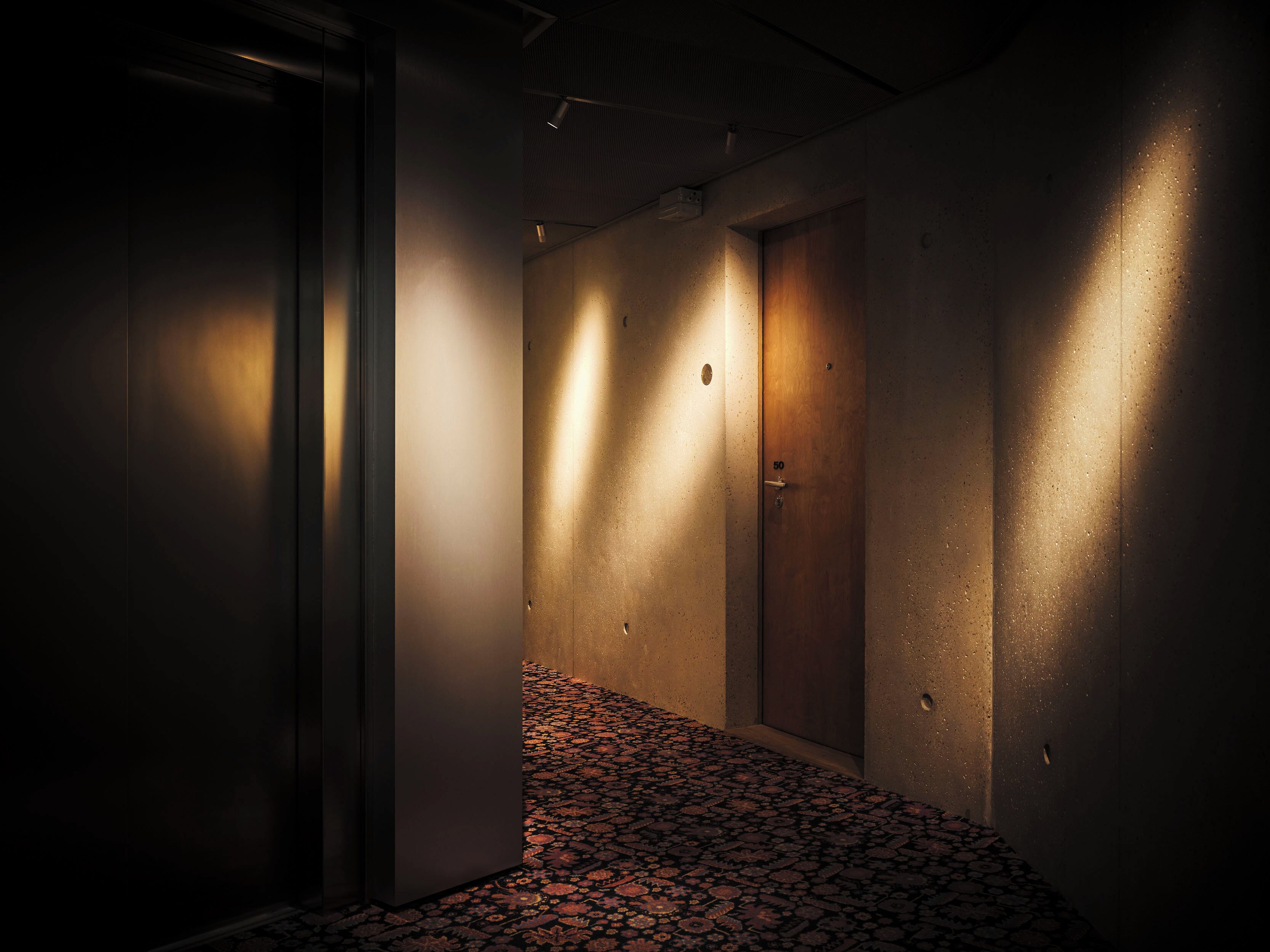 A narrow hallway with a patterned carpet, two doors, and a light source on the right wall.