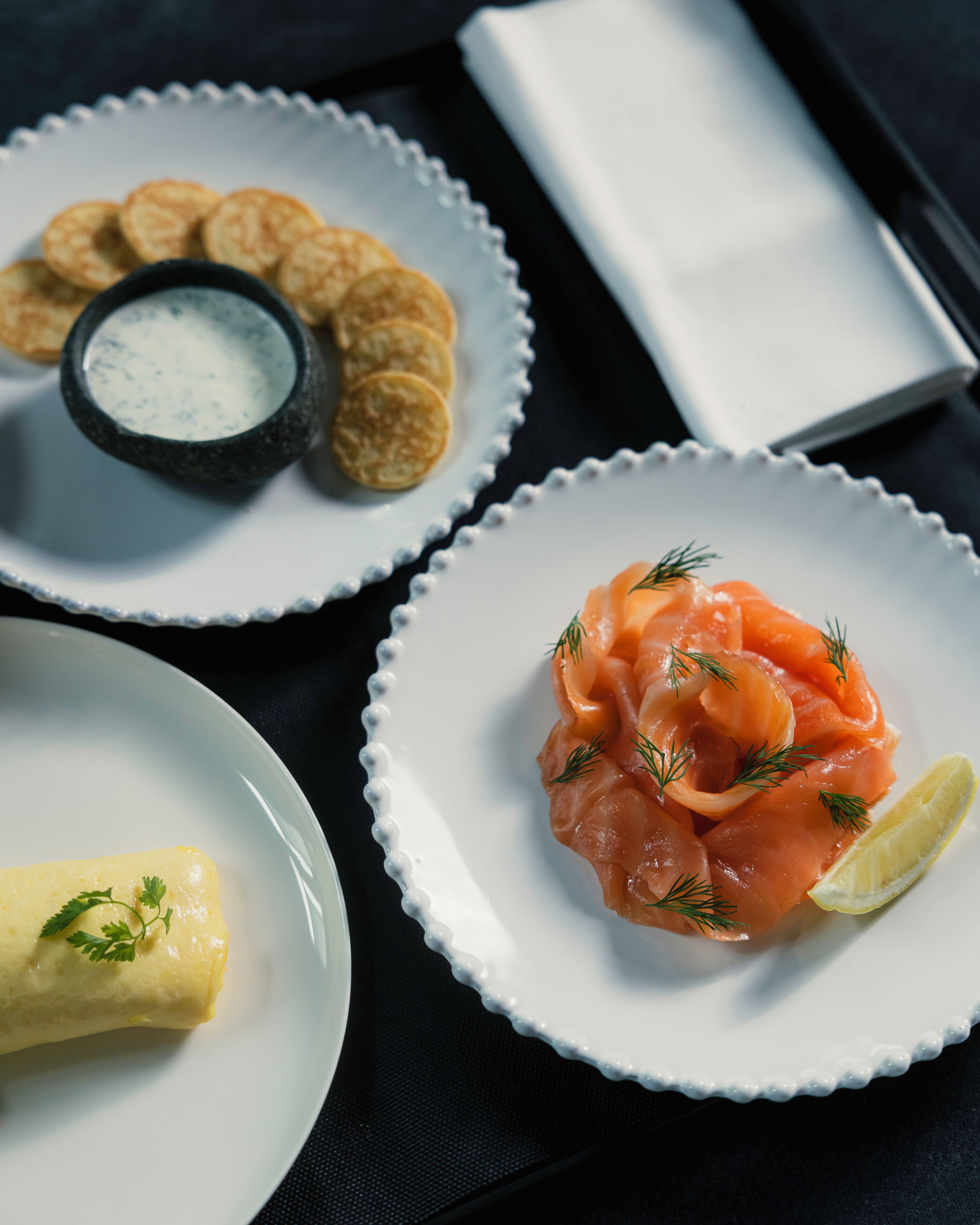 Tres platos de comida con salmón, un bol de salsa y una servilleta sobre una mesa.