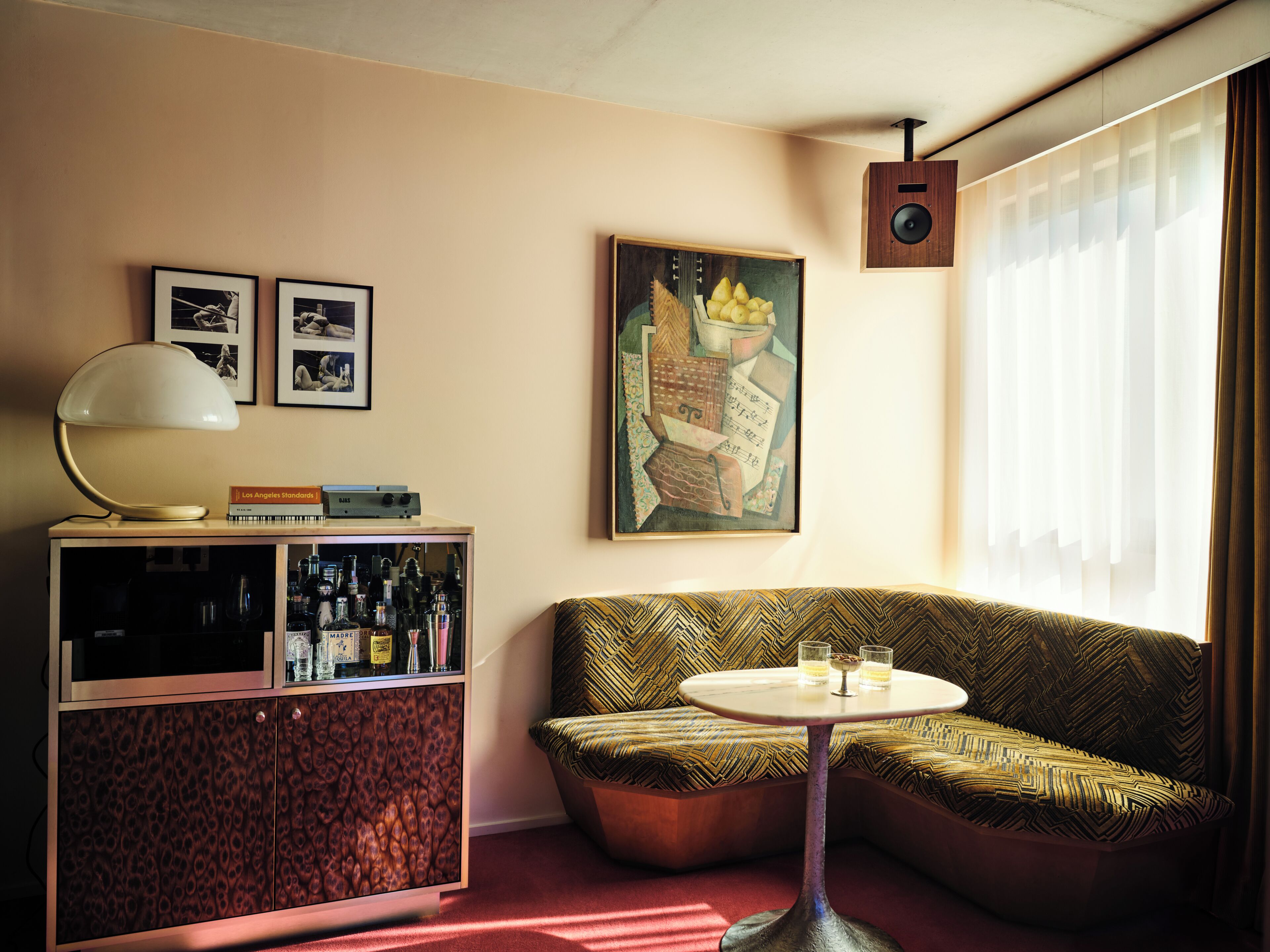 Una habitación con sofá, una mesita, un mueble con botellas, cuadros en la pared y un altavoz.