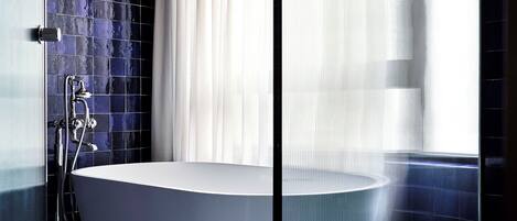 A modern bathroom with a freestanding bathtub, a glass shower enclosure, and a tiled wall.