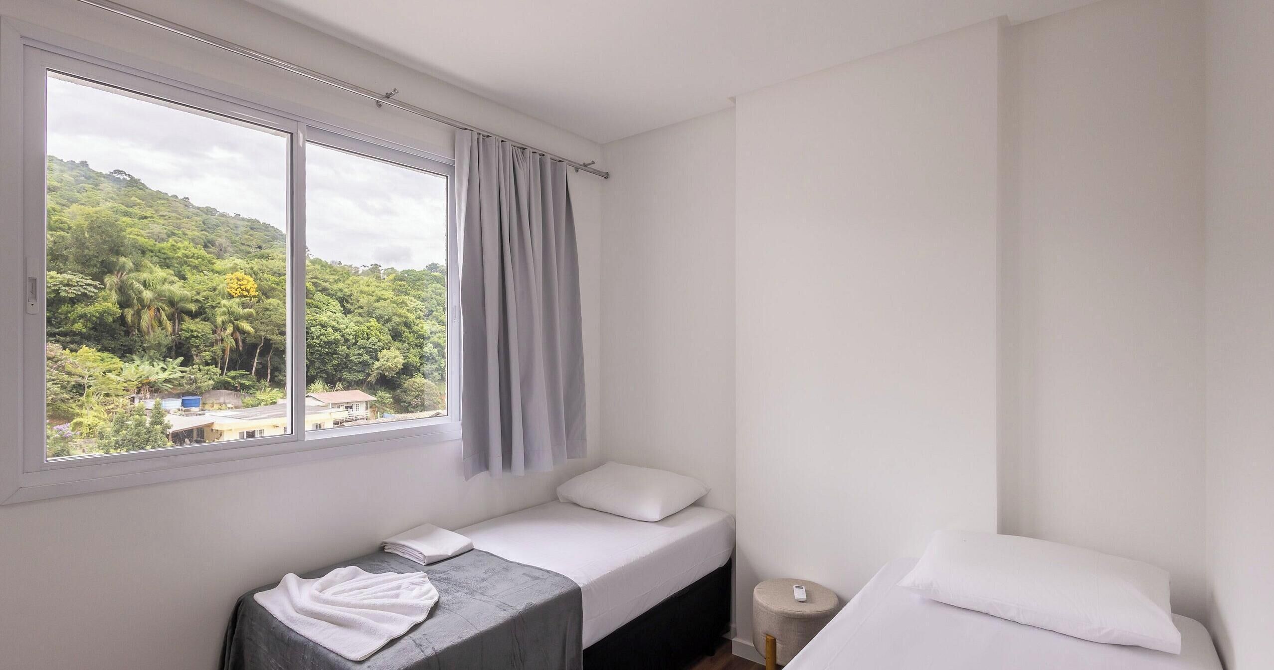 A small, clean room with a bed, a bench, and a window offering a view of a green landscape.