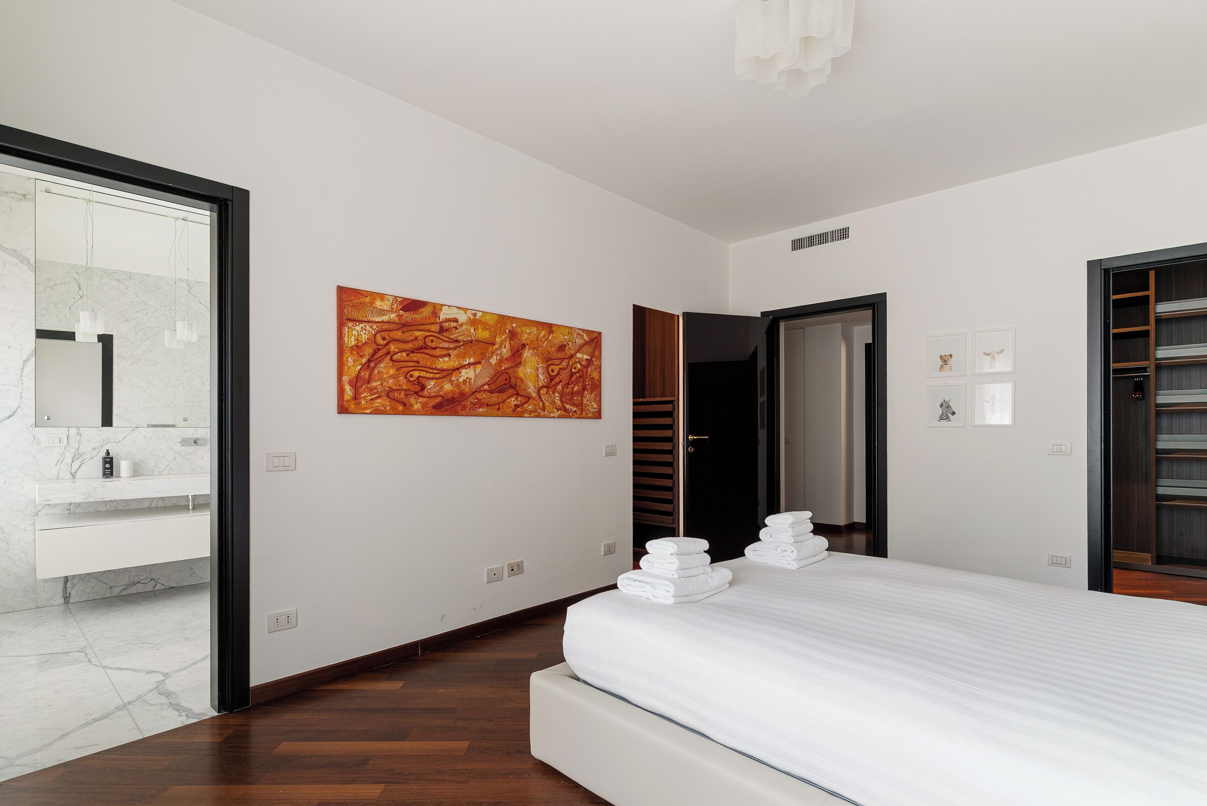 Quarto de hotel moderno com uma cama grande, banheiro com toucador de mármore e uma pintura abstrata grande na parede.