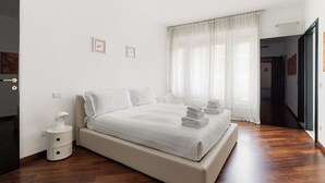 A modern bedroom with a large bed, a bedside table, and a window with sheer curtains. - Brera Apartments in Dateo (Milan)