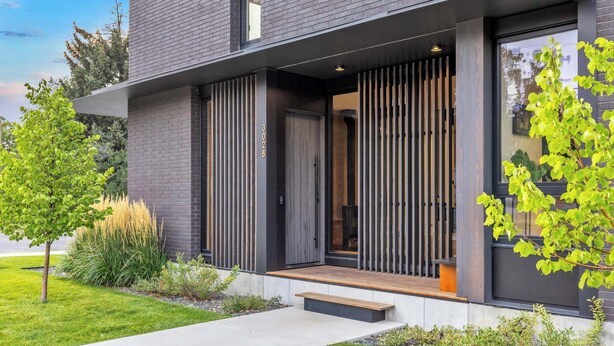 A modern two-story building with a dark brick exterior, large windows, and a wooden deck.