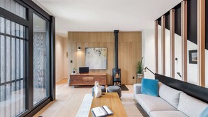 A modern living room with a wooden coffee table, a sofa, a fireplace, and a large window.