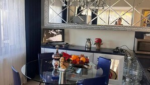Un comedor con mesa de vidrio, sillas azules, una araña y un espejo decorativo.