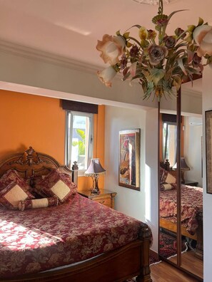 Un dormitorio con una cama grande, una mesita de noche, una lámpara, un espejo y una ventana con cortinas.
