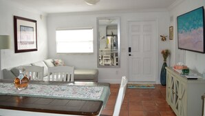 Una sala de estar con un sofá, una mesa de comedor con una botella, un mueble y un cuadro en la pared.