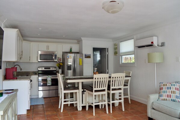 Cocina compacta con armarios blancos, microondas, refrigerador y comedor con mesa y sillas.