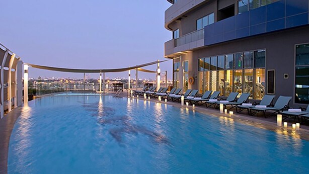 Ein Pool mit Liegestühlen und Blick auf die Stadt im Abendlicht.