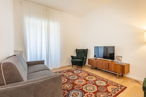 Una sala de estar con sofá, un sillón verde, un televisor sobre un mueble de madera y una alfombra estampada.