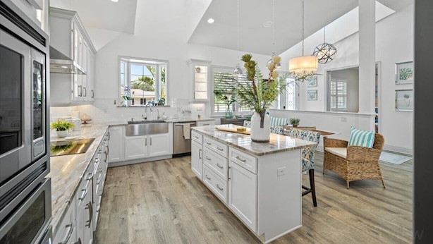 A spacious kitchen with white cabinetry, a large island, and a dining area with wicker furniture.