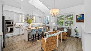 A modern kitchen with white cabinets, a central island, bar stools, and a chandelier.