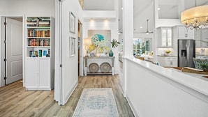 A modern kitchen with a built-in refrigerator, a dining area with a white table, and a bookshelf filled with books.