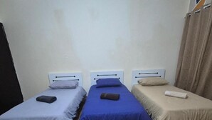 Une chambre avec trois lits simples alignés côte à côte, chacun étant muni d’une tête de lit et d’un oreiller.
