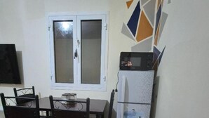 Un petit coin repas avec une table et des chaises, un réfrigérateur et une fenêtre à vitrage dépoli.