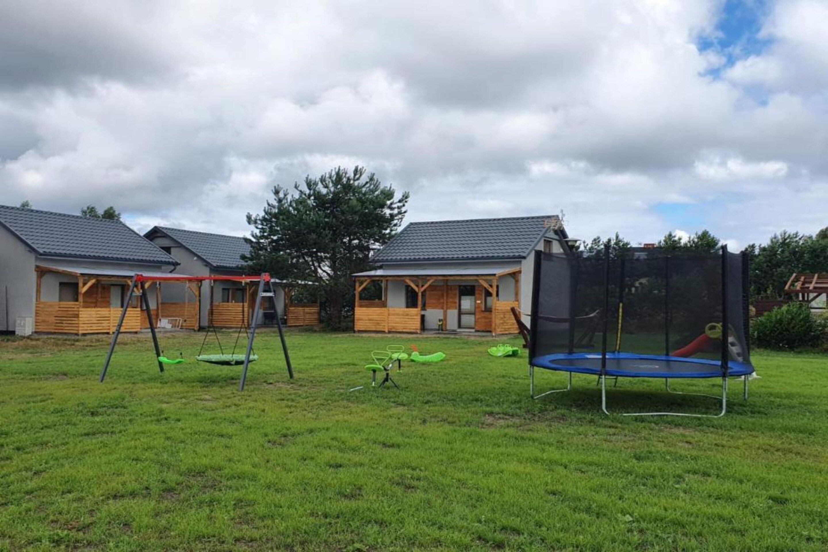 A grassy outdoor area with a swing set, a trampoline, and a wooden building with a sloped roof.