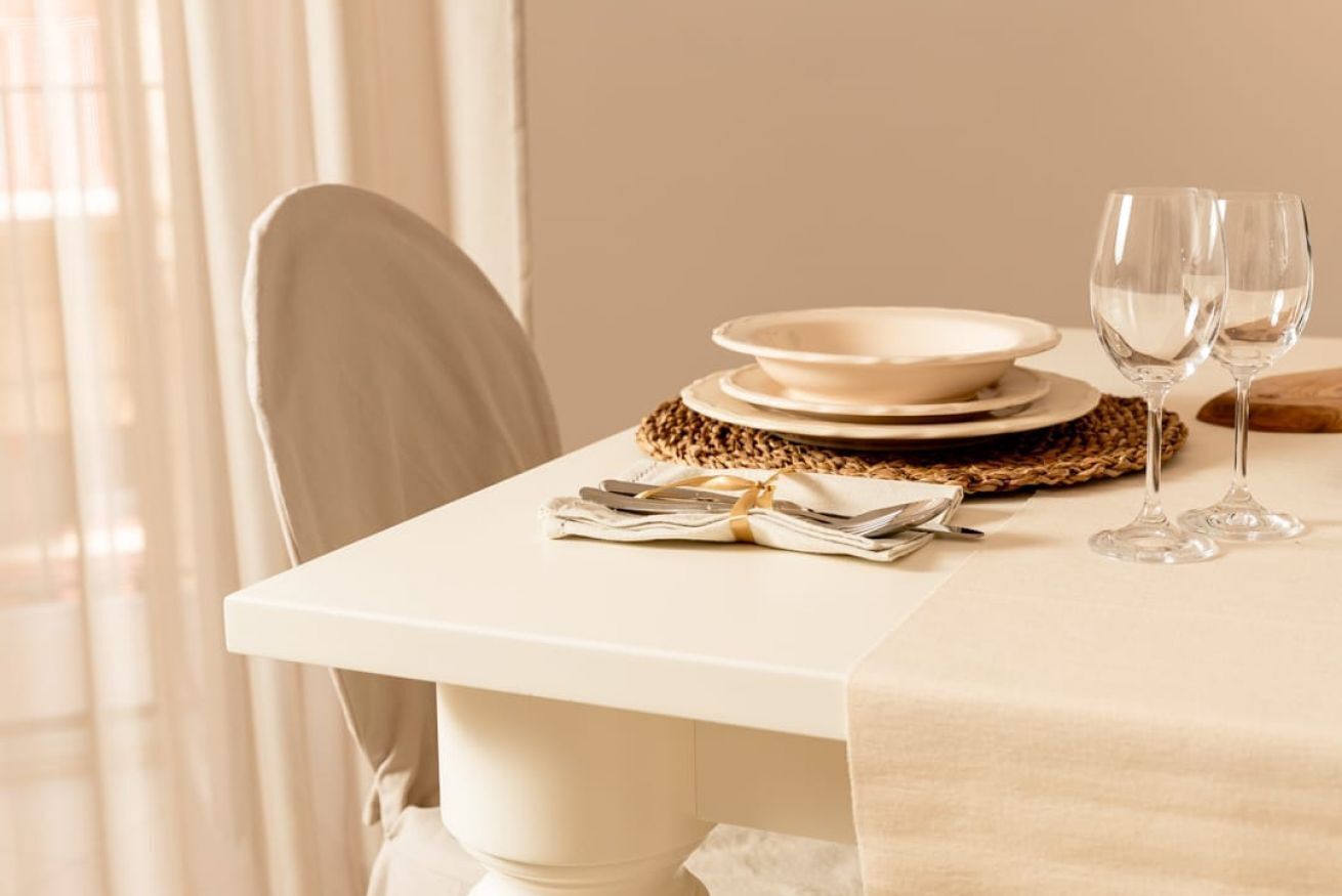 A dining table set with plates, cutlery, and glasses, with a woven placemat underneath.