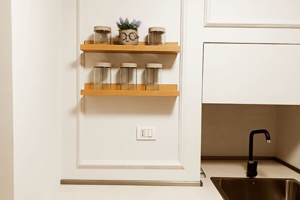 A kitchen with white cabinetry, a black faucet, and three wooden shelves with glass jars and a potted plant.