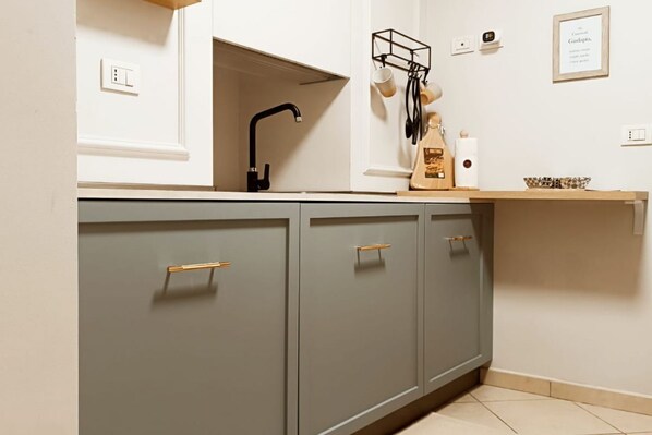 A kitchen with grey cabinets, a black faucet, a wooden shelf with kitchenware, and a framed quote on the wall.