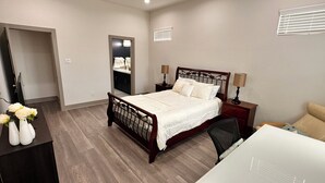 A bedroom with a bed, bedside tables, a desk, a chair, a mirror, and a dresser.