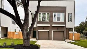 A modern two-story building with a garage, a covered driveway, and a well-maintained lawn.