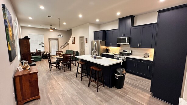 A modern kitchen with dark cabinets, a central island, and a dining area with a green couch.